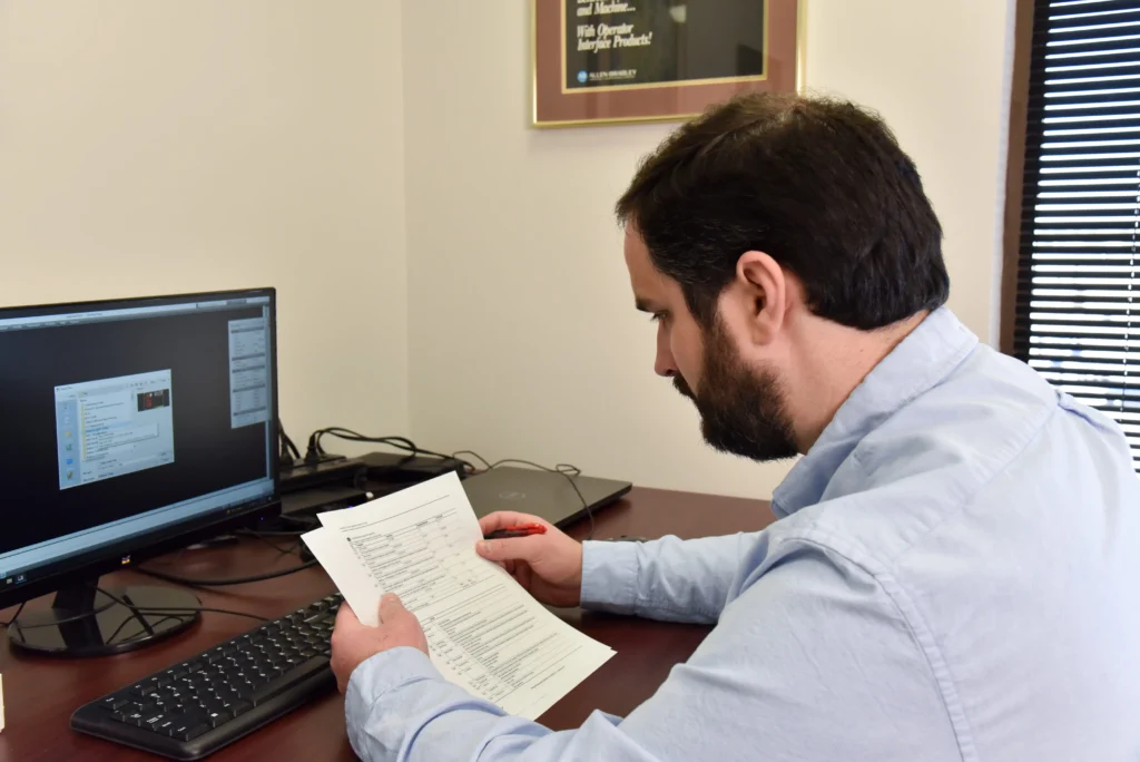 Industrial automation specialist reviewing system documentation and workflow data at a computer workstation.